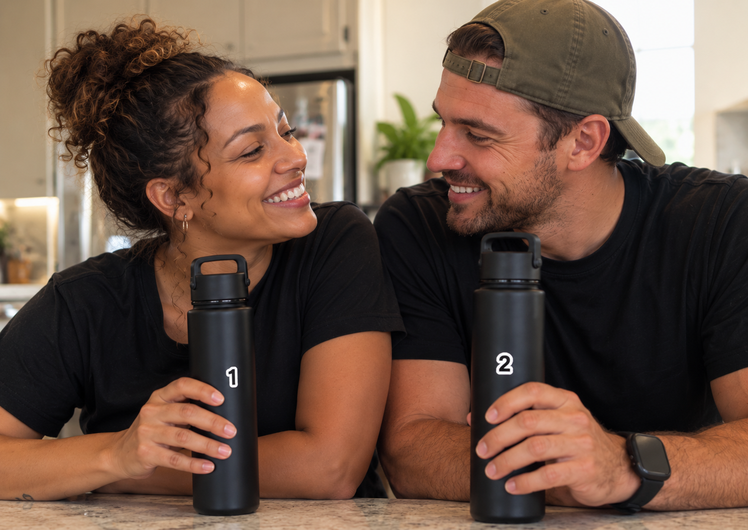 Couple smiling at each other in their kitchen, each holding a matching black water bottle, tagged 1 and 2
